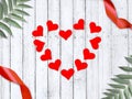 Love greeting composition with frame made red hearts, ribbons and palm leaves on wooden background.