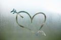 Love heart with arrow on a wet window. Closeup on foggy glass background