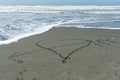 A love heart drawn in the sand is pierced with cupid`s arrow