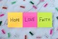 Love, hope, and faith handwritten words on colorful notes with decorative clothespins on white marble background