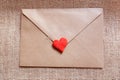 Love letter in a craft envelope with clay red heart on a jute background