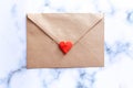 Love letter in a craft envelope with clay red heart on marble background