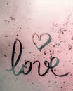 Love lettering with a symbol heart drawn with a finger on a pink misted frosty glass with glare of the sun, a symbol of happy love