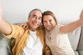 Love lives forever. Happy senior spouses taking selfie, enjoying spending time together while sitting on sofa Royalty Free Stock Photo