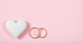 Close up and top view of golden wedding rings and a white heart, , copy space, on a pink background. Royalty Free Stock Photo