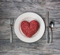 A love of meat, fresh ground beef in the shape of a heart on a white plate with cutlery and grey wood background Royalty Free Stock Photo