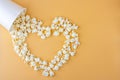 Love movies concept. Popcorn in paper box scattered on orange background heart shaped top view, copy space for text. Cinema snack