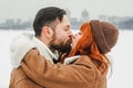 Love romantic couple lovestory. Brutal bearded man, bright red-haired girl woman in winter park. Romantic date, kissing Royalty Free Stock Photo