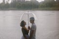 Love story of funny couple walking near river in hard rainfall with umbrella. cute man and woman in white skirt, yellow sweater Royalty Free Stock Photo