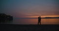 Love story on the sunset. Sillhouetes of man and woman kissing each other tender while they stand on the shore in the