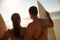 Love together, surf together. Rearview shot of a young surfer couple looking out at the beach and distant waves.