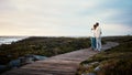 Love, travel and elderly couple hug on a boardwalk at a beach, calm and content against blue sky background. Senior, man