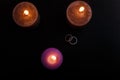 Love triangle and broken relationship concept. Wedding rings and three burning candles on black background. Flat lay Royalty Free Stock Photo