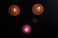 Love triangle and broken relationship concept. Wedding rings and three burning candles on black background. Royalty Free Stock Photo