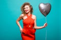 Love woman smiling holding red heart shaped balloon. Cute beautiful young woman in love. Caucasian female model in red dress isola Royalty Free Stock Photo