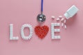 LOVE word made from medicine pills, red heart shape pouring out of white bottle and stethoscope, on pink background. Royalty Free Stock Photo