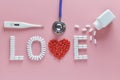 LOVE word made from medicine pills, red heart shape pouring out of white bottle and stethoscope, temperature, on pink background. Royalty Free Stock Photo