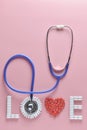 LOVE word made from medicine pills, red heart shape and stethoscope, on pink background. Royalty Free Stock Photo