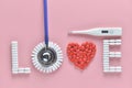 LOVE word made from medicine pills, red heart shape and stethoscope, temperature, on pink background. Concept of Valentine`s Day Royalty Free Stock Photo