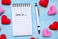 LOVE IS... word on note book and pen with red and pink heart shape decoration on blue wooden table background. Wedding, Romantic Royalty Free Stock Photo