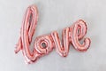 Love word from pink inflatable balloon on grey concrete background. The concept of romance, Valentine`s Day. Love rose gold foil Royalty Free Stock Photo