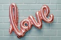 Love word from pink inflatable balloon on mint tile wall background. The concept of romance, Valentine`s Day. Love rose gold foil Royalty Free Stock Photo