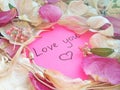 Love you message on pink sticky note with dry rose and orchid flower petals and jewelry ring and chain on wooden background Royalty Free Stock Photo