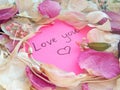 Love you message on pink sticky note with dry rose and orchid flower petals and silver jewelry ring and chain on wooden back Royalty Free Stock Photo