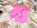 Love you message on pink sticky note with dry rose and orchid flower petals on wooden table background Royalty Free Stock Photo