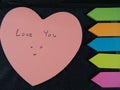 Love you with smiling face, drawing and writing on pose its paper with colorful heart and arrow on black leatherette background