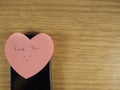 Love you with smiling face writing on sticker note and black mobile phone on wood background Royalty Free Stock Photo