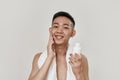 Love your skin. Portrait of shirtless young asian man with towel around his neck looking at camera, applying lotion Royalty Free Stock Photo