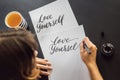 Love yourself. Calligrapher Young Woman writes phrase on white paper. Inscribing ornamental decorated letters