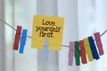 Love yourself first. A note on sticky notes hanging on rope with colorful clips on white background Royalty Free Stock Photo