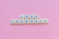 Love yourself message made with board game letters, over a soft pink background Royalty Free Stock Photo