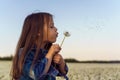 Loveable girl carefully hold white dandelion and blowing seeds of flower, walking in field. Tassels flying through air.