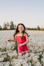 Loveable little girl in pink jumpsuit running across field full of white dandelions and smiling happily, enjoying time. Royalty Free Stock Photo