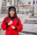 Lovely admirable ravishing calm girl in black kepi holds her red overcoat by hands and smiles