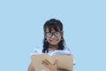 Lovely adorable charming asian little girl wearing glasses and writing information on her notebook isolated on blue background. Royalty Free Stock Photo