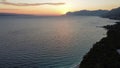 Aerial view of a calm sea surrounded by hills at sunset with the red sun going under mountains Royalty Free Stock Photo