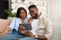 Lovely African American couple sitting on sofa, using tablet Royalty Free Stock Photo