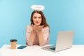 Lovely angelic woman employee with nimbus sitting at workplace and sending air kiss to camera Royalty Free Stock Photo