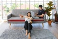 Lovely Asian couple in living room at home. young woman with headphone sit on floor playing video game, man lying on couch working Royalty Free Stock Photo