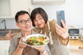 A lovely Asian couple taking pictures or selfies with their food in the kitchen together Royalty Free Stock Photo