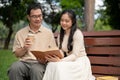 A lovely Asian daughter enjoys reading a book with her dad while relaxing in a green park together Royalty Free Stock Photo