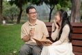 A lovely Asian daughter enjoys reading a book with her dad while relaxing in a green park together