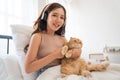 Lovely Asian girl with headphone hold and cudding orange cat and sit on bed also look at camera with smiling and day light Royalty Free Stock Photo