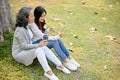 Lovely Asian granddaughter and grandmother sitting under the tree in the green park together Royalty Free Stock Photo