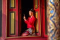 Lovely Asian Thai woman wear Thai Lanna traditional style sit at the red door of ancient building and look at bracelet or ornament Royalty Free Stock Photo