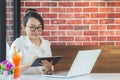 Lovely Asian woman wearing glasses sitting at coffee shop with laptop. and tablet Royalty Free Stock Photo